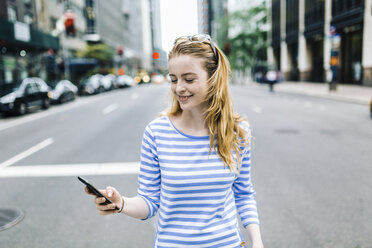 USA, New York, Manhattan, Young woman walking in the street, holding mobile phone - GIOF01889