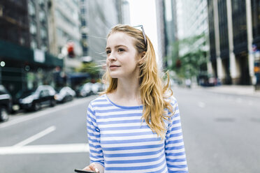 USA, New York, Manhattan, Junge Frau geht auf der Straße, hält Handy - GIOF01891