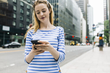 USA, New York, Manhattan, Young woman walking in the street, holding mobile phone - GIOF01893