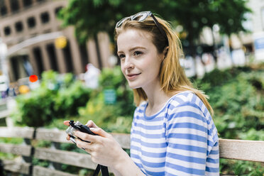 Young woman sitting on bench, holding camera - GIOF01896