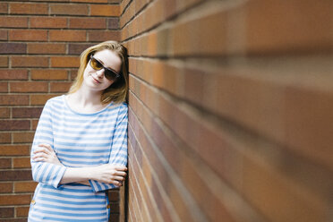 Porträt einer jungen Frau, die sich an eine Backsteinmauer lehnt - GIOF01899
