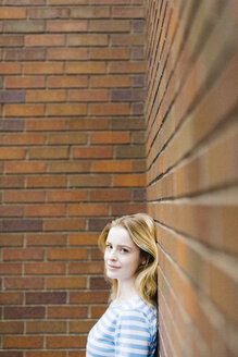 Porträt einer jungen Frau, die sich an eine Backsteinmauer lehnt - GIOF01900