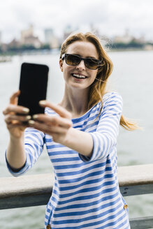 USA, New York City, Junge Frau steht in Manhattan und macht ein Selfie - GIOF01905