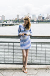 USA, New York City, Junge Frau steht in Manhattan und benutzt ein Smartphone - GIOF01906