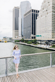 USA, New York City, Junge Frau steht in Manhattan an einem Geländer und hält ein Smartphone in der Hand - GIOF01911