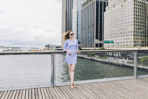 USA, New York City, Young woman standing in Manhattan at railing, holding smart phone stock photo