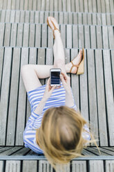 Junge Frau sitzt am Pier und benutzt ein Mobiltelefon - GIOF01916