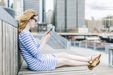 Young woman sitting at pier using mobile phone - GIOF01917