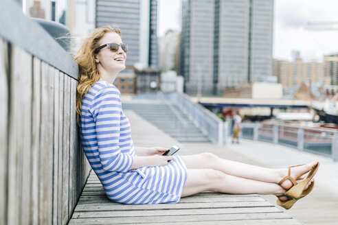 Junge Frau sitzt am Pier und benutzt ein Mobiltelefon - GIOF01918