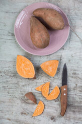 Geschnittene und ganze Süßkartoffeln, Teller und Küchenmesser auf Holz - JUNF00851