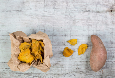 Süßkartoffelchips und frische Süßkartoffeln auf Holz, lizenzfreies Stockfoto