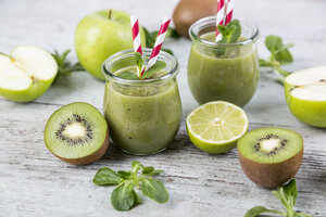 Zwei Gläser mit grünem Smoothie und Zutaten auf Holz - JUNF00859