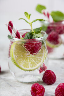 Glass of detox water with limes and rasperries decorated with mint leaves - JUNF00866