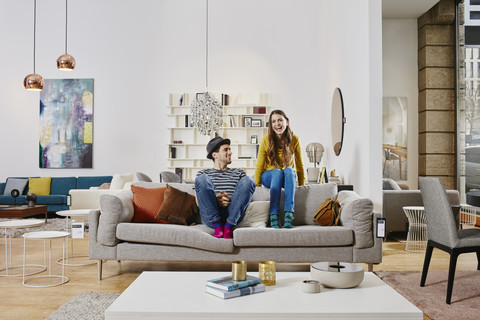 Paar in einem modernen Möbelhaus sitzt auf einer Couch und lacht, lizenzfreies Stockfoto