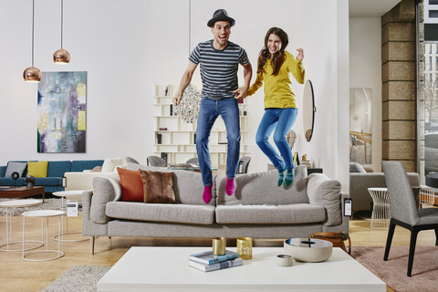 Pärchen in modernem Möbelhaus springt auf Couch, lizenzfreies Stockfoto