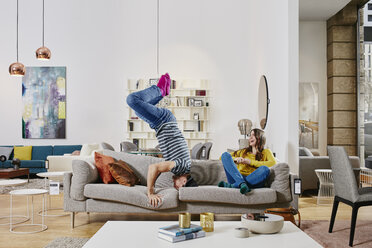Couple in modern furniture store doing headstand on couch - RORF00596