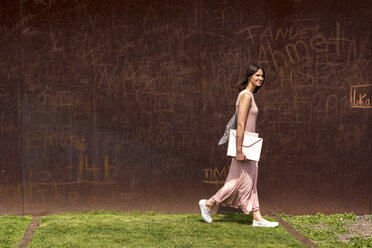 Smiling young woman walking in front of corten wall - LMF00633