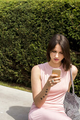 Junge Frau sitzt auf einer Bank und benutzt ein Smartphone - LMF00638