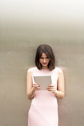 Young woman leaning against metal wall using tablet - LMF00645