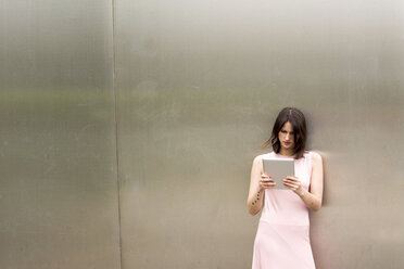 Young woman leaning against metal wall using tablet - LMF00646