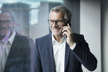 Lächelnder Geschäftsmann mit Mobiltelefon am Fenster - RBF05616