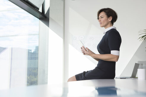 Businesswoman with tablet in office looking out of window - RBF05631