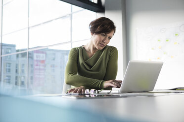 Businesswoman using laptop in office - RBF05635