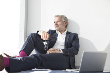 Businessman sitting on the floor next to laptop - RBF05640