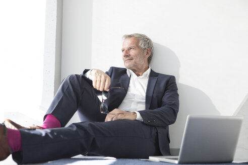 Businessman sitting on the floor next to laptop - RBF05640