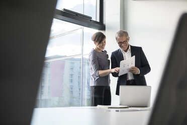 Smiling businessman and businesswoman looking at documents in office - RBF05645