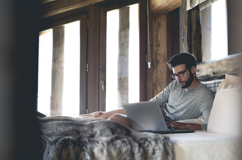 Junger Mann mit Laptop im Bett liegend zu Hause, lizenzfreies Stockfoto