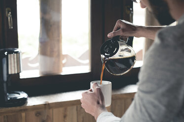 Young man pouring coffee into cup at home - ZOCF00152