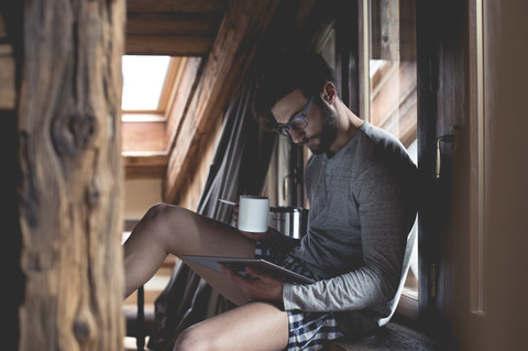 Young man using tablet and drinking coffee at home stock photo