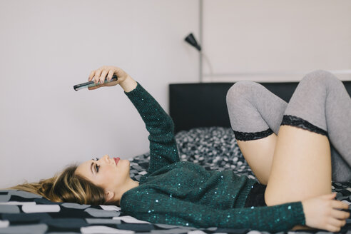 Young woman lying on bed using cell phone - LCUF00089