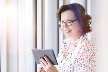 Lächelnde ältere Geschäftsfrau mit Tablet am Fenster - MMAF00035