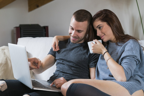 Junges Paar sitzt auf der Couch und benutzt einen Laptop, lizenzfreies Stockfoto