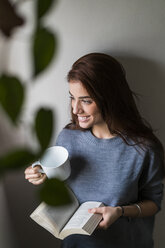 Attractive young woman reading book and drinking coffee - KKAF00471