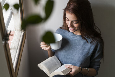 Attraktive junge Frau liest ein Buch und trinkt Kaffee - KKAF00472