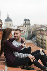 Amorous couple sitting on rooftop, kissing and ambracing - KKAF00484