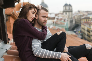 Amorous couple sitting on rooftop, kissing and ambracing - KKAF00485