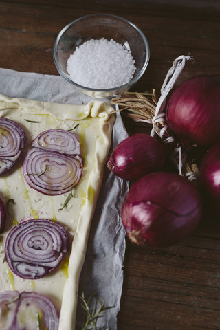 Zubereitete ungebackene Focaccia, garniert mit roten Zwiebeln und Rosmarin auf Papier, lizenzfreies Stockfoto