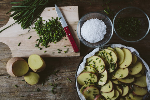 In Scheiben geschnittene Kartoffeln mit Schnittlauch, roten Pfefferkörnern und Salz in der Backform, lizenzfreies Stockfoto