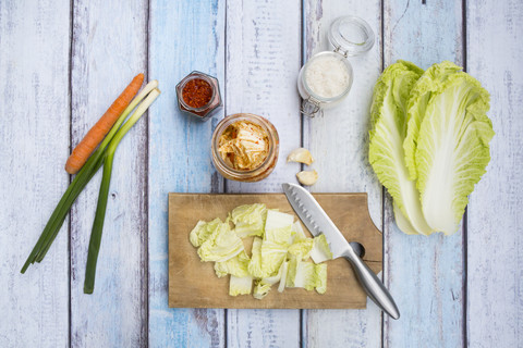 Glas mit Kimchi, Zutaten, Holzbrett und Küchenmesser auf Holz, lizenzfreies Stockfoto