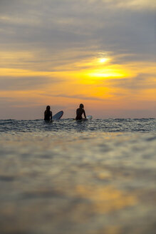 Indonesien, Bali, zwei Surferinnen im Meer bei Sonnenuntergang - KNTF00634