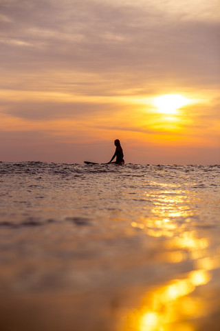 Indonesien, Bali, Surferin im Meer bei Sonnenuntergang, lizenzfreies Stockfoto