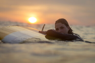 Indonesia, Bali, portrait of female surfer in the ocean at sunset - KNTF00642