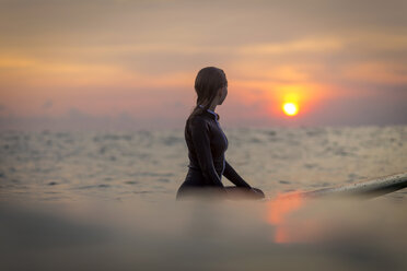 Indonesia, Bali, female surfer in the ocean at sunset - KNTF00644