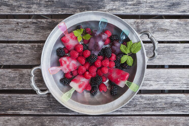 Tin plate of homemade lemonade ice lollies with raspberries and blackberries - GWF04997