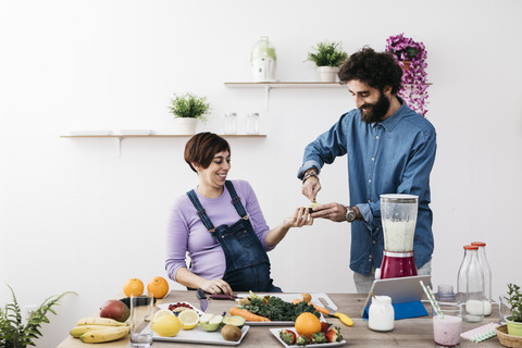 Lächelndes ccouple bei der Zubereitung gesunder Smoothies mit frischem Obst und Gemüse, lizenzfreies Stockfoto