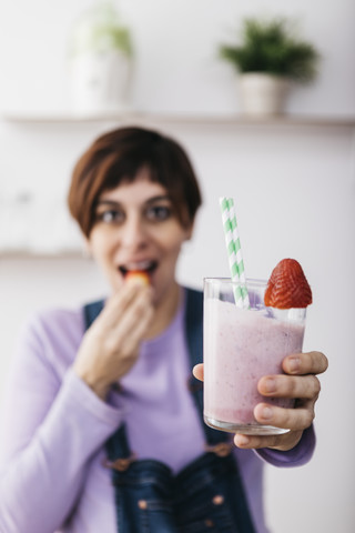 Frau hält ein Glas mit Erdbeer-Smoothie und isst eine Frucht, lizenzfreies Stockfoto